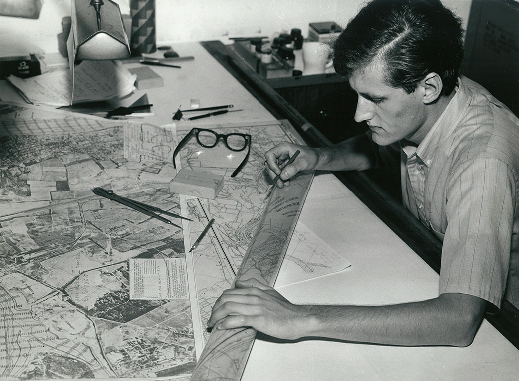 A professional drawing carefully across a large table, an image of patient work where every assumption has to be tested and every choice owned.